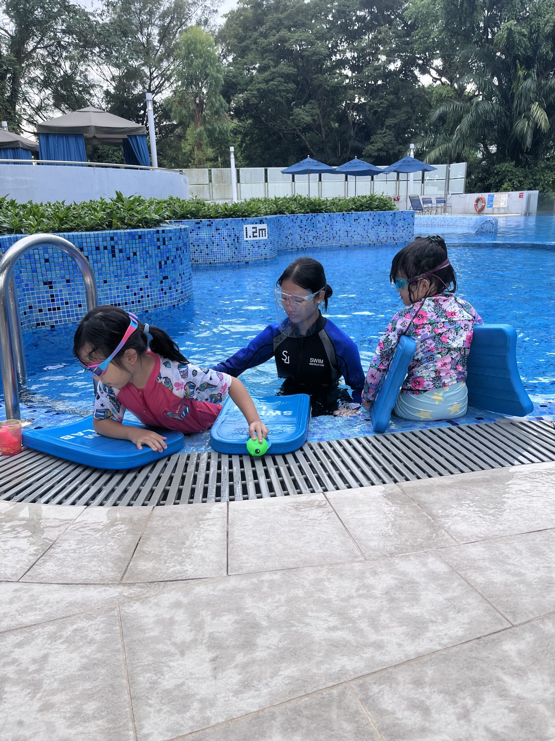 Coach guiding two children during a swimming lesson in a pool.