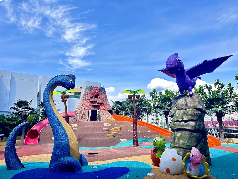 A dinosaur-themed water play area with a volcano slide entrance, located next to Cantine by Kopitiam